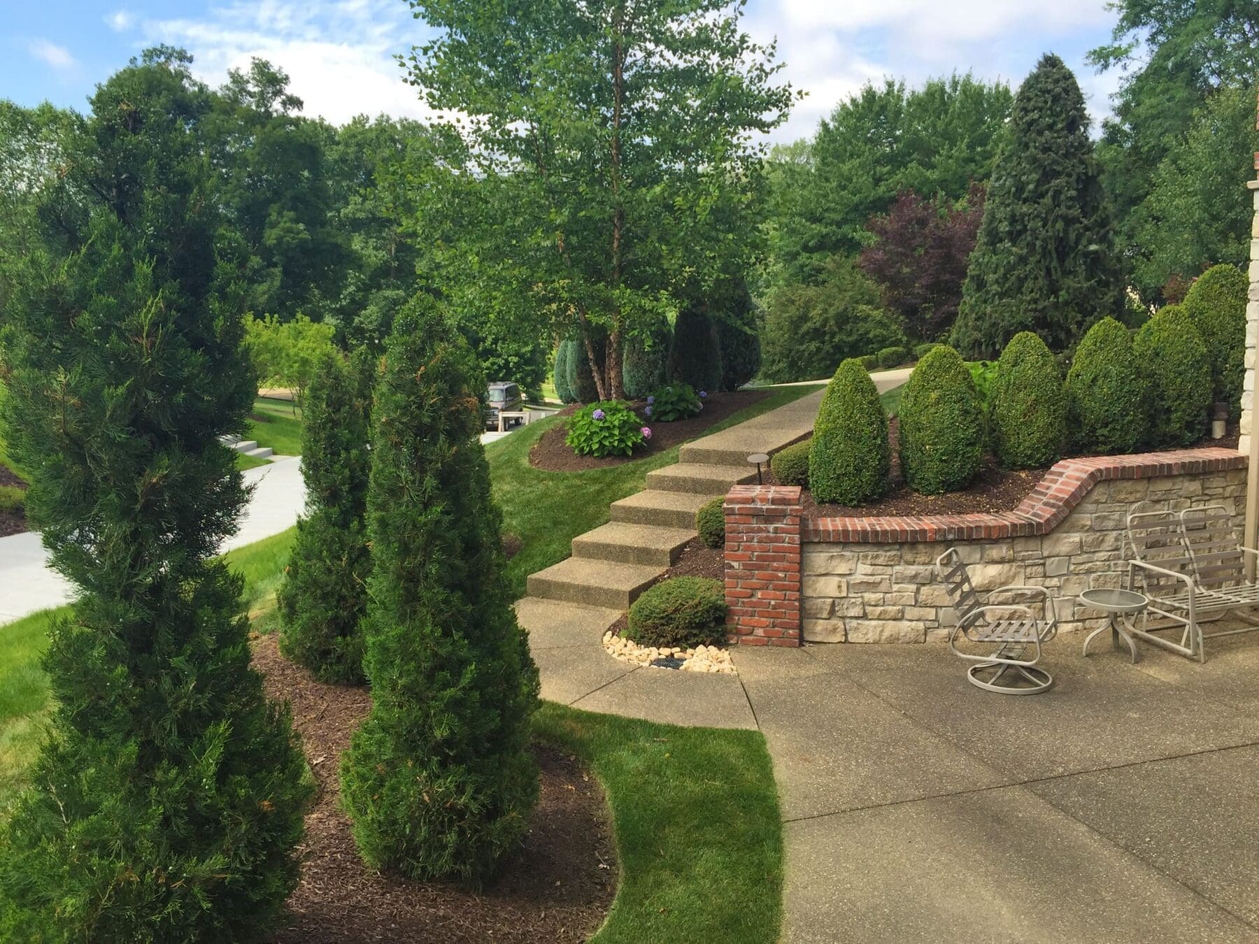 Neatly pruned evergreens and shaped shrubs lining a walkway on a sloped South Hills property