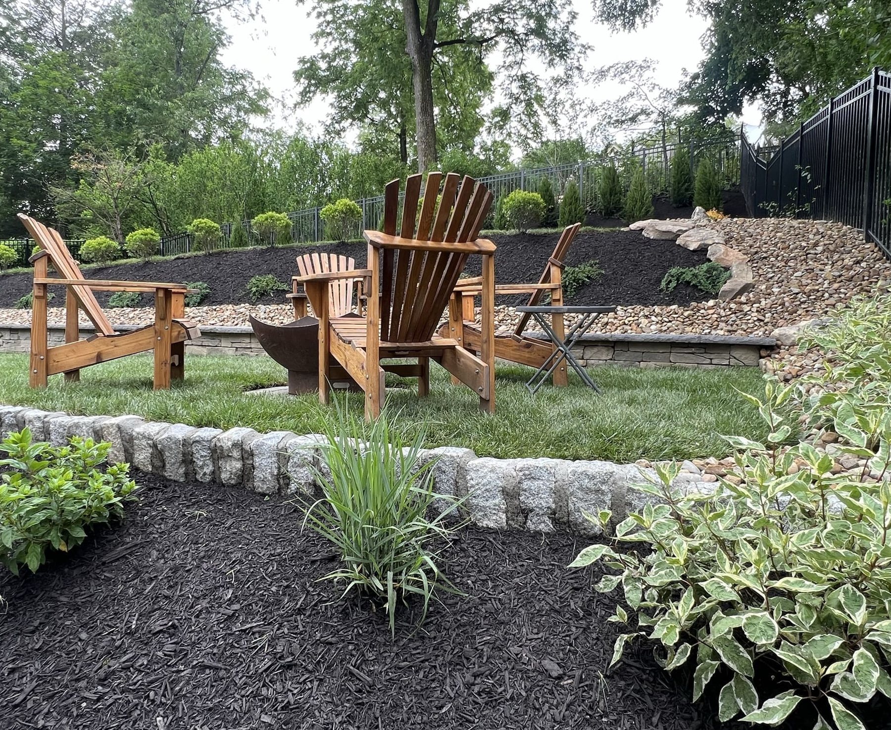 Adirondack chairs in a landscaped backyard seating area with stone edging