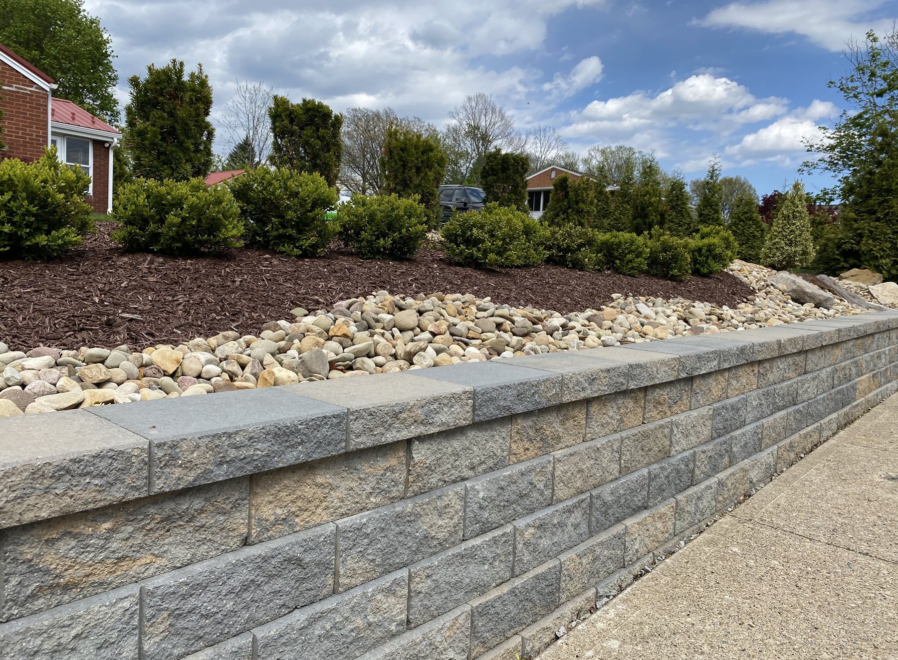 Segmental retaining wall topped with river rock and shrubs