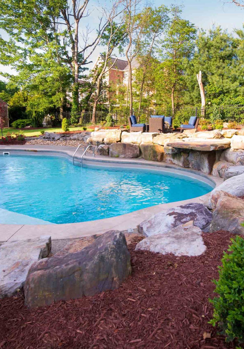 Backyard pool surrounded by boulder accents and mulched planting beds