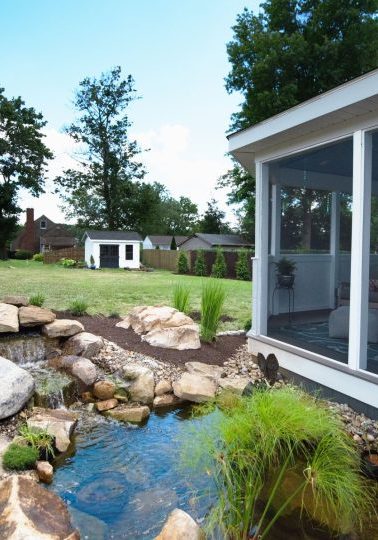 Screened gazebo beside a landscaped pond with boulders